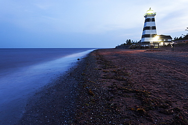 Illuminated West Point Lighthouse seen from empty beach, Prince Edward Island, New Brunswick, Canada