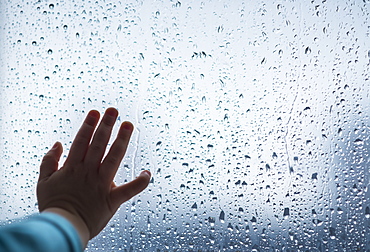 Close-up of girl's hand on wet window