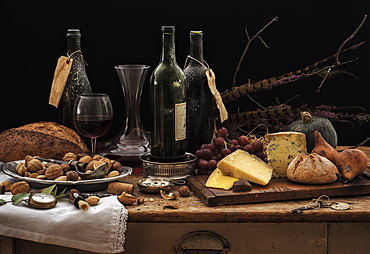 Still life with wine bottles, selection of cheese, bread and nuts on wooden table, studio shot