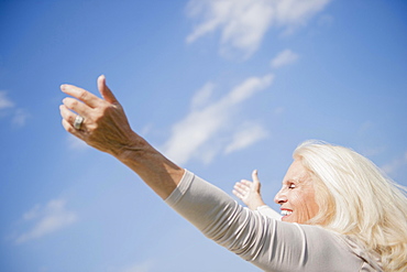 Senior woman with arms outstretched against sky