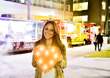 Woman in front of building and food truck holding illuminated heart, Jupiter, Florida