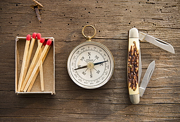 Studio Shot of matchsticks, compass and knife on wooden board