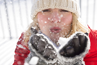 Portrait of woman wearing knit hat blowing snow