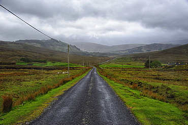 Landscape with asphalt road and green grass, clouds in sky, hills in background, Rural County Mayo, Ireland