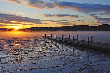 Jetty on frozen lake, hills in background at sunrise, Lake George, New York