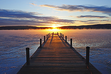 Symmetrical view of jetty on frozen lake, hills in background at sunrise, Lake George, New York