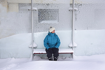 Middle aged woman sitting in bus stop, winter snow, Boston, Massachusetts 