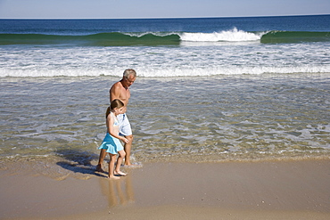 Father and daughter walking in ocean surf