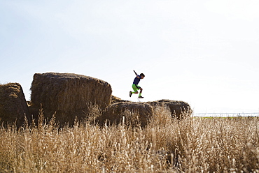 Boy (6-7) jumping on bale of hay