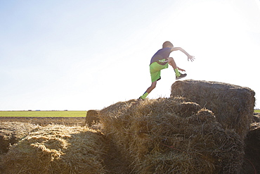 Boy (6-7) jumping on bale of hay