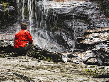 Australia, New South Wales, Blue Mountains, Mid-adult man crouching at foot of waterfall