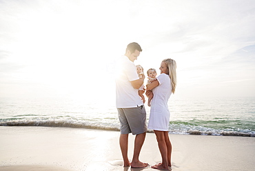 Happy family with two baby girls (2-5 months) at beach in sunlight