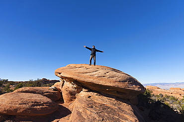 Man with arms outstretched on rock in Arches National Park, Utah, USA