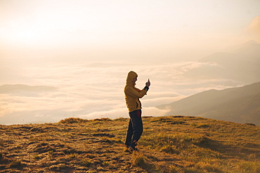 Man in yellow jacket taking photograph on smart phone in the Carpathian Mountain Range