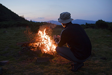 Man crouching by campfire