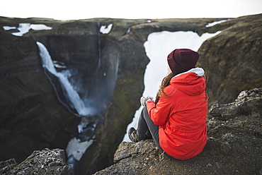 Hiker sitting on cliff by Haifoss waterfall in Iceland