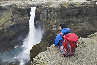 Hiker with backpack on cliff by Haifoss waterfall in Iceland