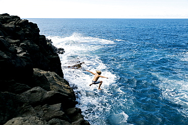 Boy jumping off cliff by sea