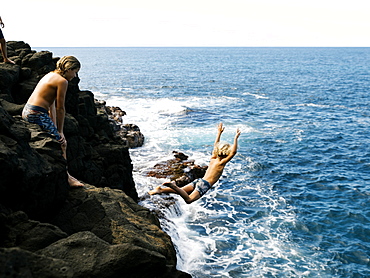 Boy jumping off cliff by sea