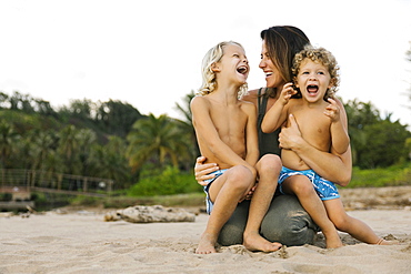 Woman with her sons sitting on her lap on beach