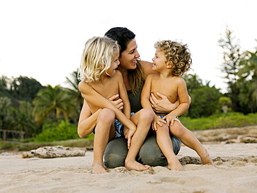 Woman with her sons sitting on her lap on beach