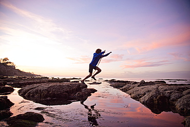 Teenage boy jumping between rocks of tide pool in La Jolla, California