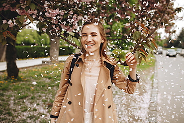 Smiling woman among falling petals from tree in bloom