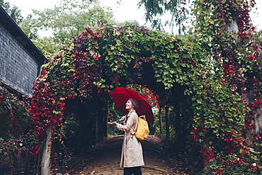 Woman holding umbrella by vine covered arch