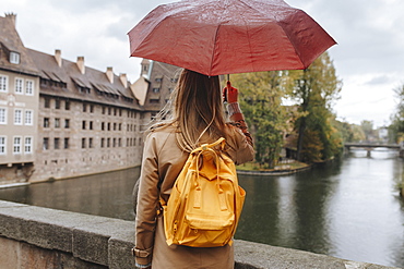 Woman wearing backpack holding umbrella by river in Nuremberg, Germany