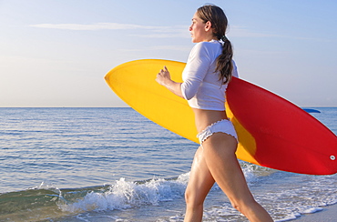 Woman holding surfboard running into sea