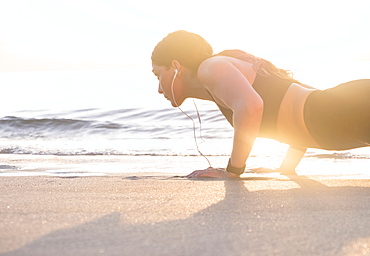 Woman wearing headphones doing push-up on beach