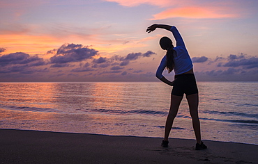 Woman practicing yoga on beach at sunset