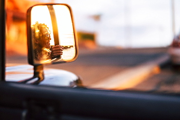 Reflection in wing mirror of smiling woman wearing sunglasses