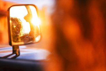 Reflection in wing mirror of smiling woman wearing sunglasses