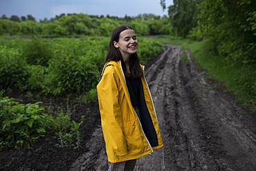 Smiling teenage girl wearing yellow raincoat on country road