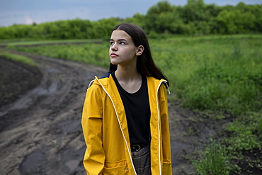 Teenage girl wearing yellow raincoat on country road