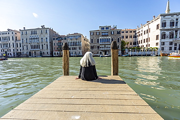 Woman sitting on jetty on Grand Canal in Venice, Italy