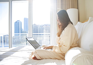 Woman wearing bathrobe using laptop while on phone call