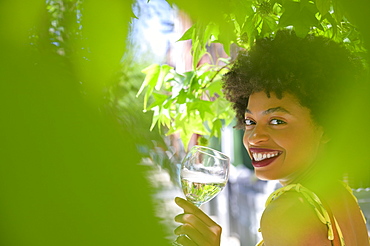 Smiling young woman with glass of white wine under tree