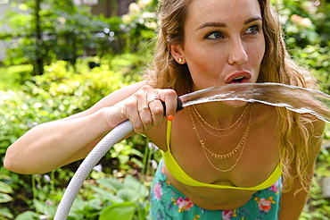 Young woman drinking from garden hose