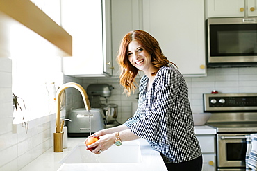 Smiling woman washing apple in kitchen sink