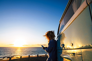 Woman using smart phone by beach at sunset in Fuerteventura, Canary Islands