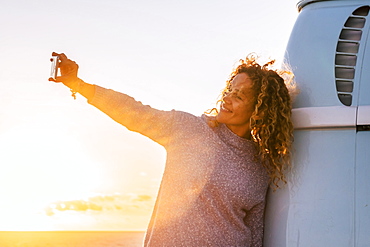 Woman taking selfie by camper van at sunset