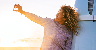 Woman taking selfie by camper van at sunset