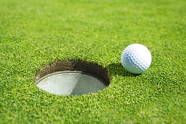 Golf ball near cup on putting green outdoors