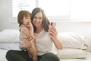 Mother and daughter taking selfie on bed