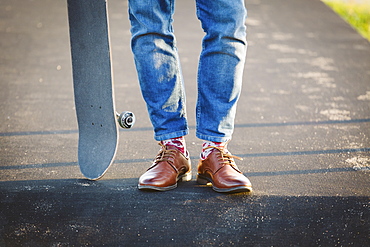 Feet of man with skateboard on footpath
