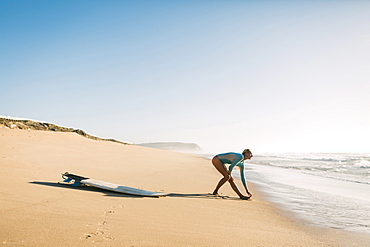 Woman wearing wetsuit stretching on beach