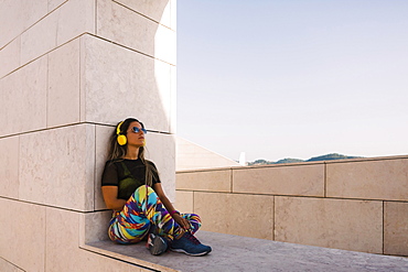 Woman wearing headphones sitting on wall