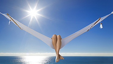 Woman's legs hanging over side of hammock at beach